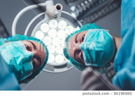From below female surgeons in medical uniform using professional tools while standing under bright From below female surgeons in medical uniform using professional tools while standing under bright 86196860