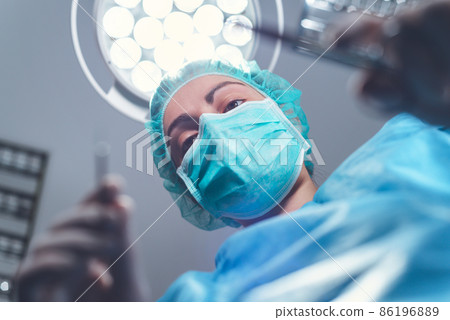 From below woman surgeon in medical uniform using professional tools while standing under bright 86196889