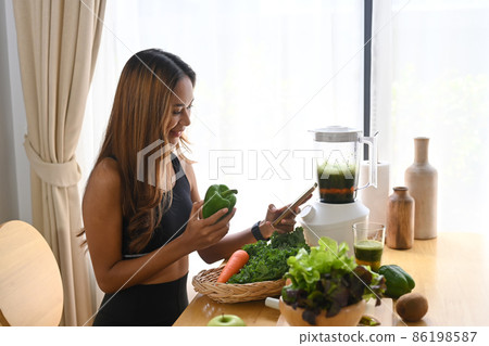 Happy asian woman using smart phone and making healthy green vegetable smoothie at home. 86198587