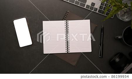 Top view of minimal workplace with blank screen smartphone, copy space on notebook Top view of minimal workplace with blank screen smartphone, copy space on notebook 86199934