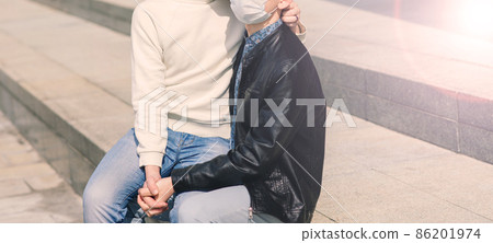 Young gay couple wearing medical mask, hugging and kissing at the city. Young gay couple wearing medical mask, hugging and kissing at the city. 86201974