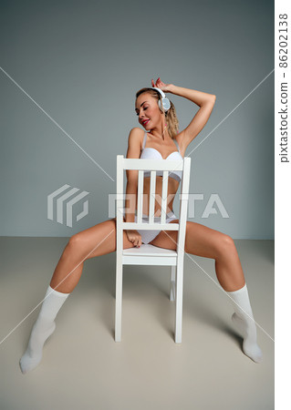 Banner of young happy girl in white swimsuit listening to music in white chair, wearing wireless headhones, isolated on gray background with copy space in studio Banner of young happy girl in white swimsuit listening to music in white chair, wearing wireless headhones, isolated on gray background with copy space in studio 86202138