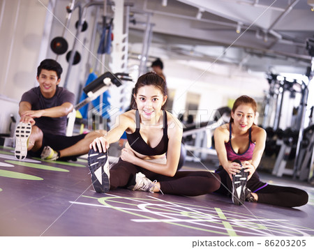 three young asian adult people exercising in gym stretching legs three young asian adult people exercising in gym stretching legs 86203205