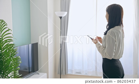 A woman who uses a smartphone in a room A woman who uses a smartphone in a room 86203437
