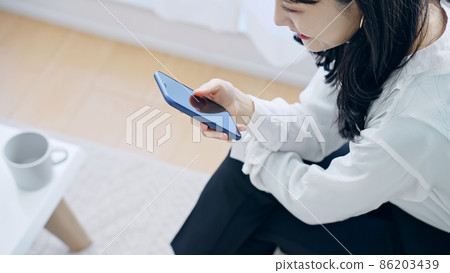 A woman who uses a smartphone in a room A woman who uses a smartphone in a room 86203439