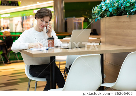Young attractive brunette woman sitting at a shopping center at a table and working at a computer Young attractive brunette woman sitting at a shopping center at a table and working at a computer 86206405
