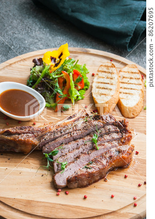 Grilled beef steak on a wooden board on a grey background. Top view. Grilled beef steak on a wooden board on a grey background. Top view. 86207695