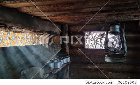 A wooden dugout in which a kerosene lamp burns. Light from the window penetrates into the room. 86208503
