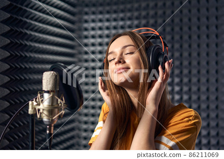 Girl in recording studio in headphones with mic over acoustic absorber panel background with closed eyes 86211069
