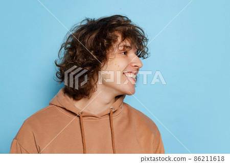 Portrait of young happy man, student in brown hoodie smiling isolated on blue background. Concept of emotions, study, education, fashion Portrait of young happy man, student in brown hoodie smiling isolated on blue background. Concept of emotions, study, education, fashion 86211618