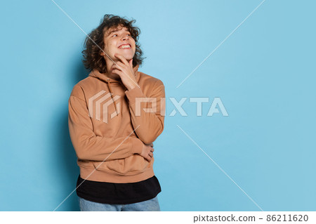 Portrait of young happy man, student in brown hoodie smiling isolated on blue background. Concept of emotions, study, education, fashion Portrait of young happy man, student in brown hoodie smiling isolated on blue background. Concept of emotions, study, education, fashion 86211620