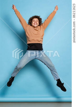 Full-length portrait of young excited man, student jumping isolated on blue background. Concept of emotions, study, education, fashion Full-length portrait of young excited man, student jumping isolated on blue background. Concept of emotions, study, education, fashion 86211623