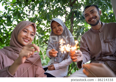 smiling father, mother and daughter lighting fireworks together 86214338