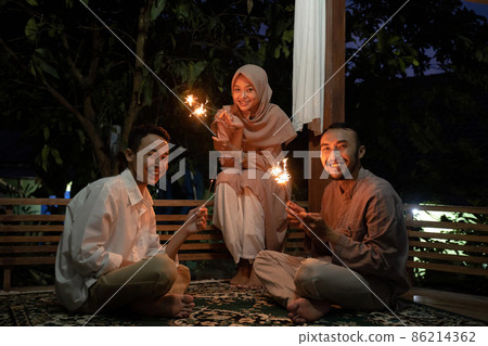 A woman and two men light fireworks together at night A woman and two men light fireworks together at night 86214362