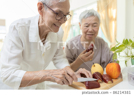 Happy asian senior grandmother cutting the fresh fruit into slices with a knife,healthy elderly people enjoy tasting delicious fruits,preparing healthy meal,cooking,healthy  food,health care concept 86214381