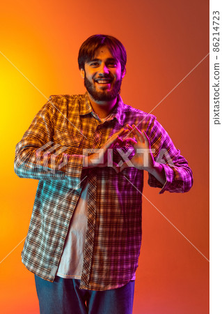 Cropped portrait of young smiling boy holding hands in heart shape and posing isolated over gradient red yellow background Cropped portrait of young smiling boy holding hands in heart shape and posing isolated over gradient red yellow background 86214723