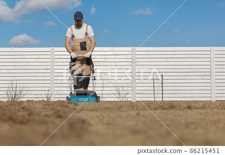 Scarifying lawn with scarifier, Man gardener scarifies the lawn and removal of old grass Scarifying lawn with scarifier, Man gardener scarifies the lawn and removal of old grass 86215451