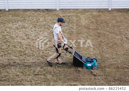 Scarifying lawn with scarifier, Man gardener scarifies the lawn and removal of old grass 86215452