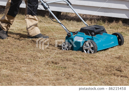 Scarifying lawn with scarifier, Man gardener scarifies the lawn and removal of old grass Scarifying lawn with scarifier, Man gardener scarifies the lawn and removal of old grass 86215458