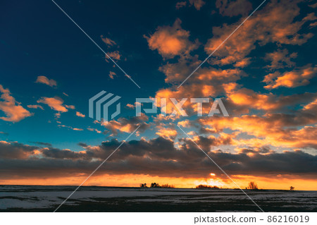 Winter Meadow Field At Evening Sunset. Natural Bright Dramatic Sky Colours Above Countryside Snowy Landscape. Agricultural Landscape In February Winter Meadow Field At Evening Sunset. Natural Bright Dramatic Sky Colours Above Countryside Snowy Landscape. Agricultural Landscape In February 86216019