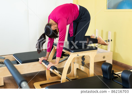 Hispanic woman performing pilates on reformer in fitness studio Hispanic woman performing pilates on reformer in fitness studio 86216703