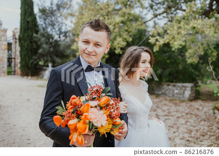 Happy stylish smiling couple walking in Tuscany, Italy on their wedding day. The bride and groom walk down the street by the hands. A stylish young couple walks. Husband and wife communicate nicely 86216876