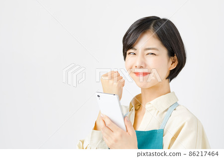 Young housewife in an apron operating a smartphone (guts pose) Young housewife in an apron operating a smartphone (guts pose) 86217464