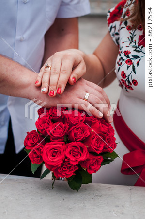 hands of newlyweds with wedding rings and bouquet with red roses 86217534