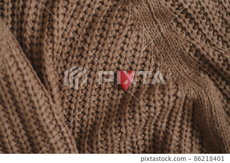Decorative red heart on beige knitted sweater. Valentines day celebration or love concept. 86218401