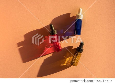 Transparent glass dropper bottles with yellow, green, red and blue liquid inside on beige background in the sunlight. Pipette with fluid hyaluronic acid, serum, retinol. Cosmetics, healthcare, beauty  86218527