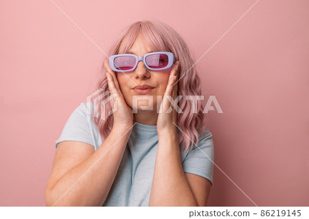 Happy young caucasian woman in bright stylish sunglasses and a blue t-shirt, smiling posing looking at the camera isolated over pink background. 86219145