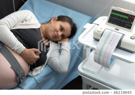 Pregnant Woman On Hospital Couch During Medical Control Cardiotocography. Gynecologist Doctor Hands Turn On Adjust CTG Device Clinic Consultant. Examine Expectant Belly Baby Mother Healthcare Check Up 86219693