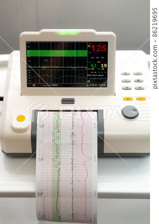 Electronic Cardiotocography Machine Monitoring Fetal Heart Contractions Of Uterus. Printing Cardiogram Report Coming Out Electrocardiogram In Labor Ward During Pregnancy. Medical Diagnostic Equipment 86219695