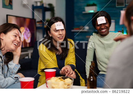 Multi-ethnic friends with stickey notes on forehead playing guess who game 86219822