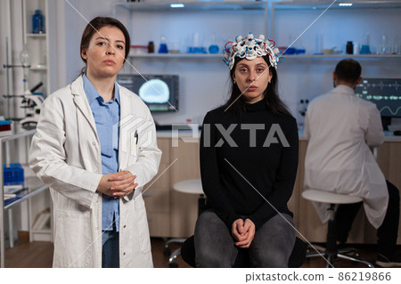Portrait of neurologist doctor standing beside woman patient with medical eeg headset Portrait of neurologist doctor standing beside woman patient with medical eeg headset 86219866