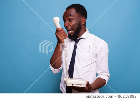 Angry businessman shouting into reciever of cord telephone arguing Angry businessman shouting into reciever of cord telephone arguing 86219882