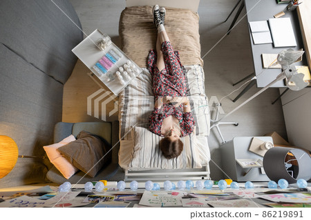 Overview of sick girl in casualwear lying on bed during medical procedure 86219891