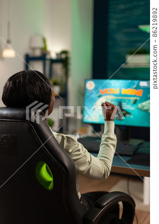 Happy excited pro gamer woman sitting at desk in gaming home studio Happy excited pro gamer woman sitting at desk in gaming home studio 86219892