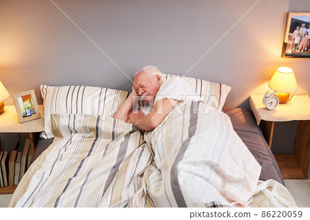Senior man lying under striped blanket on double bed 86220059