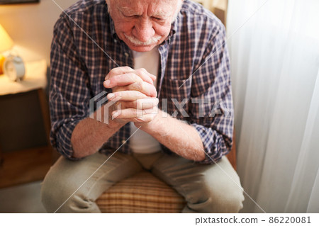 Elderly man with crossed fingers sitting on chair and praying 86220081