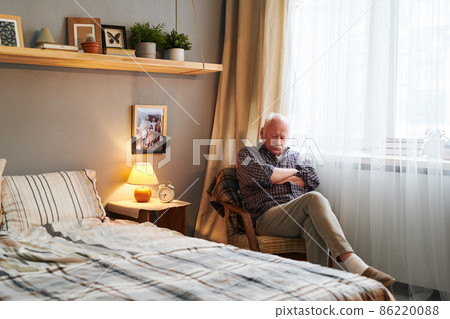 Tired senior man sitting in armchair by window and napping Tired senior man sitting in armchair by window and napping 86220088