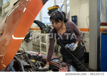 Young female worker of car maintenance service repairing vehicle 86220131