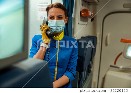 Stewardess in medical mask using telephone in aircraft cabin 86220133