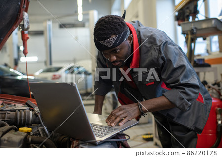 Young African repairman consulting websites while checking and repairing engine 86220178