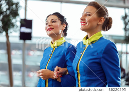 Cheerful stewardesses walking arm in arm at airport terminal Cheerful stewardesses walking arm in arm at airport terminal 86220295