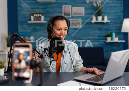 Woman vlogger with headphones looking at laptop and recording video. 86220373