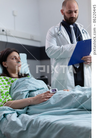 Doctor with clipboard reading medical data to patient with nasal cannula recieving oxygen 86220445