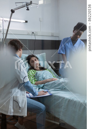 Doctor holding clipboard with lab results sitting down talking with recovering patient about treatment 86220536