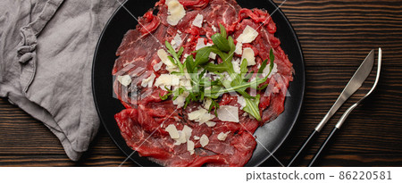 Cold meat appetizer Beef carpaccio with parmesan cheese and arugula on black plate 86220581