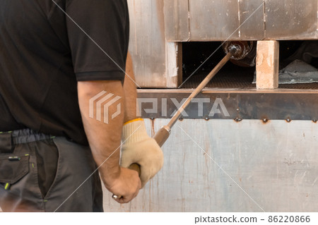 Manual glass production by glassblowing by worker at the factory. Man holding a vase in a muffle furnace. Manual glass production by glassblowing by worker at the factory. Man holding a vase in a muffle furnace. 86220866